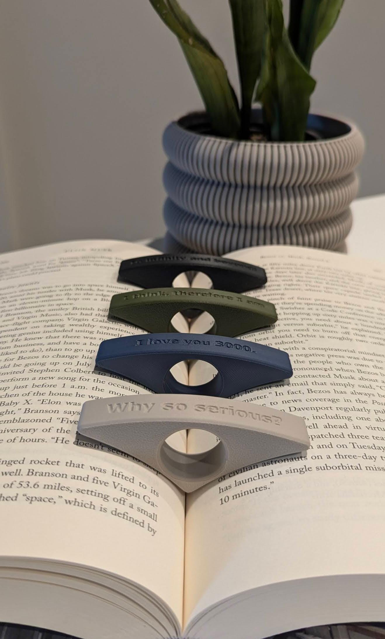 Image displaying an assortment of colorful page holders with unique text designs, with an ivory white Astria planter elegantly positioned in the background for a minimalist touch.